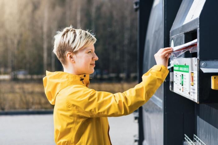 Nainen laittaa tyhjän ja puhtaan muovipakkauksen Rinki-ekopisteen muovipakkausten jäteastiaan.