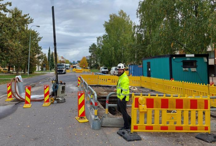 Työmies seisoo kadun reunassa työmaa-aitojen vieressä.