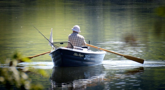 Mies soutaa soutuveneellä järvellä.