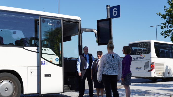 Neljä ihmistä seisoo Korsisaaren linja-auton vieressä keskustelemassa.