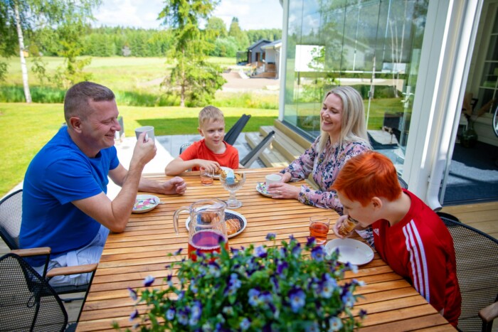 Nelihenkinen perhe istuu ulkona kahvipöydässä.