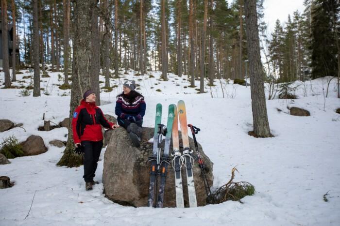 Kaksi naista metsässä, kiveen nojaavat liukulumisukset sauvoineen.