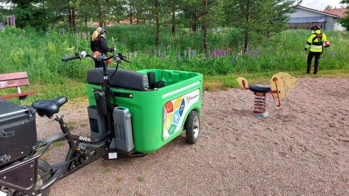 Sähköavusteinen tavarapyörä. Taustalla tyttö hävittää lupiineja.