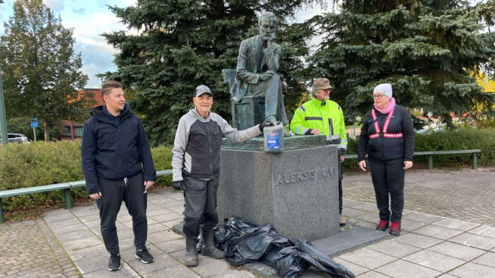 Yhdistys Kiven killan neljä ihmistä seisoo Aleksis Kiven patsaan vierellä.. Maassa siivoustalkoissa kerättyjä roskasäkkejä.